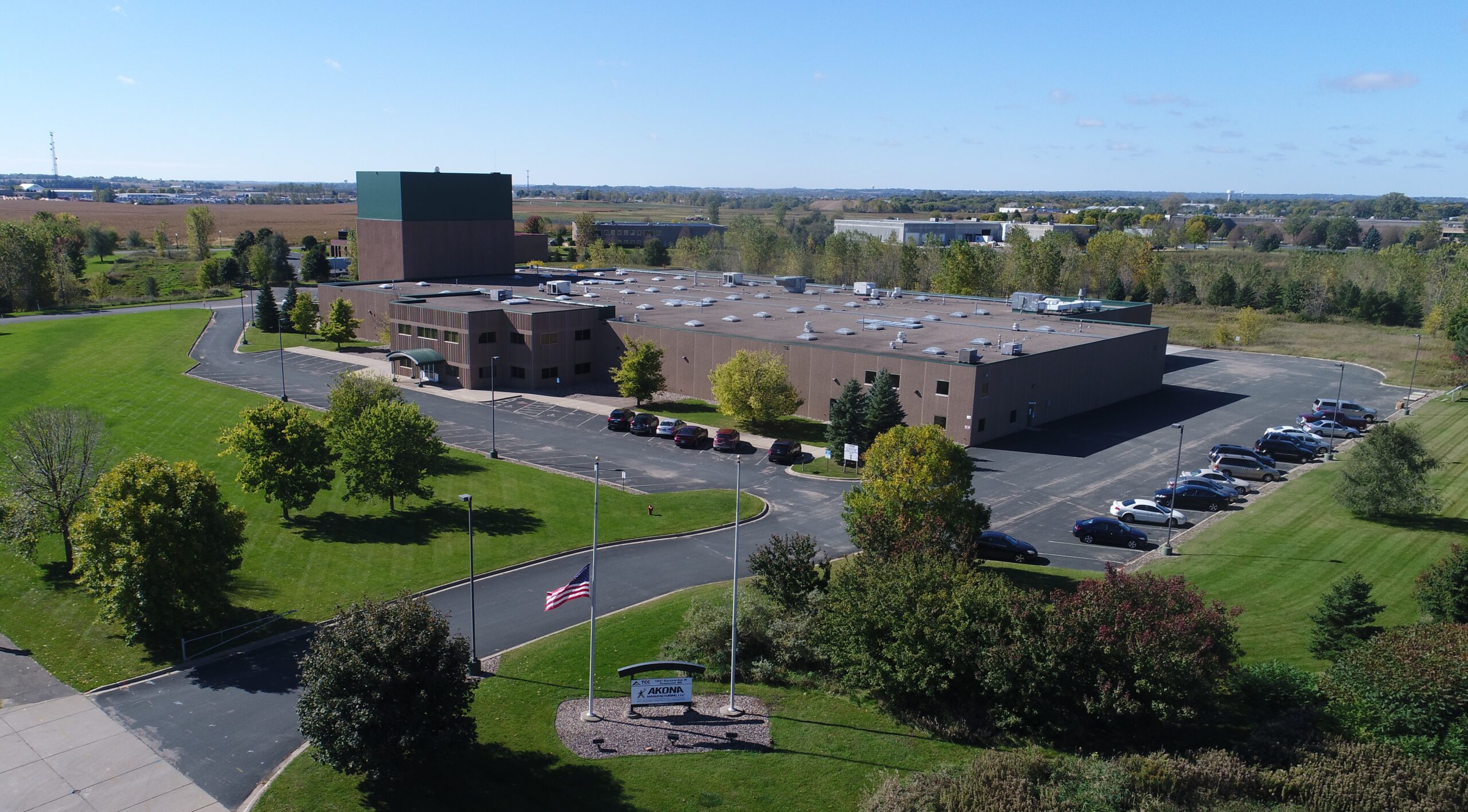Aerial view of a large brick campus building with a tall green tower, surrounded by parking lots and manicured green lawns.