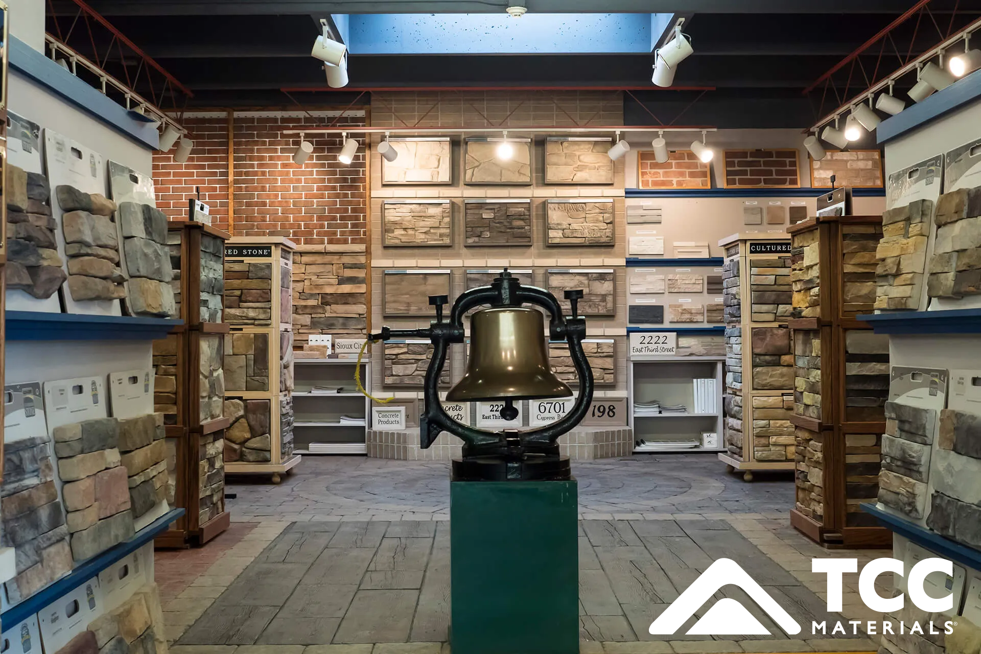 Showroom displaying stone veneer samples on shelves and brick walls, with a brass bell centerpiece on a green pedestal.
