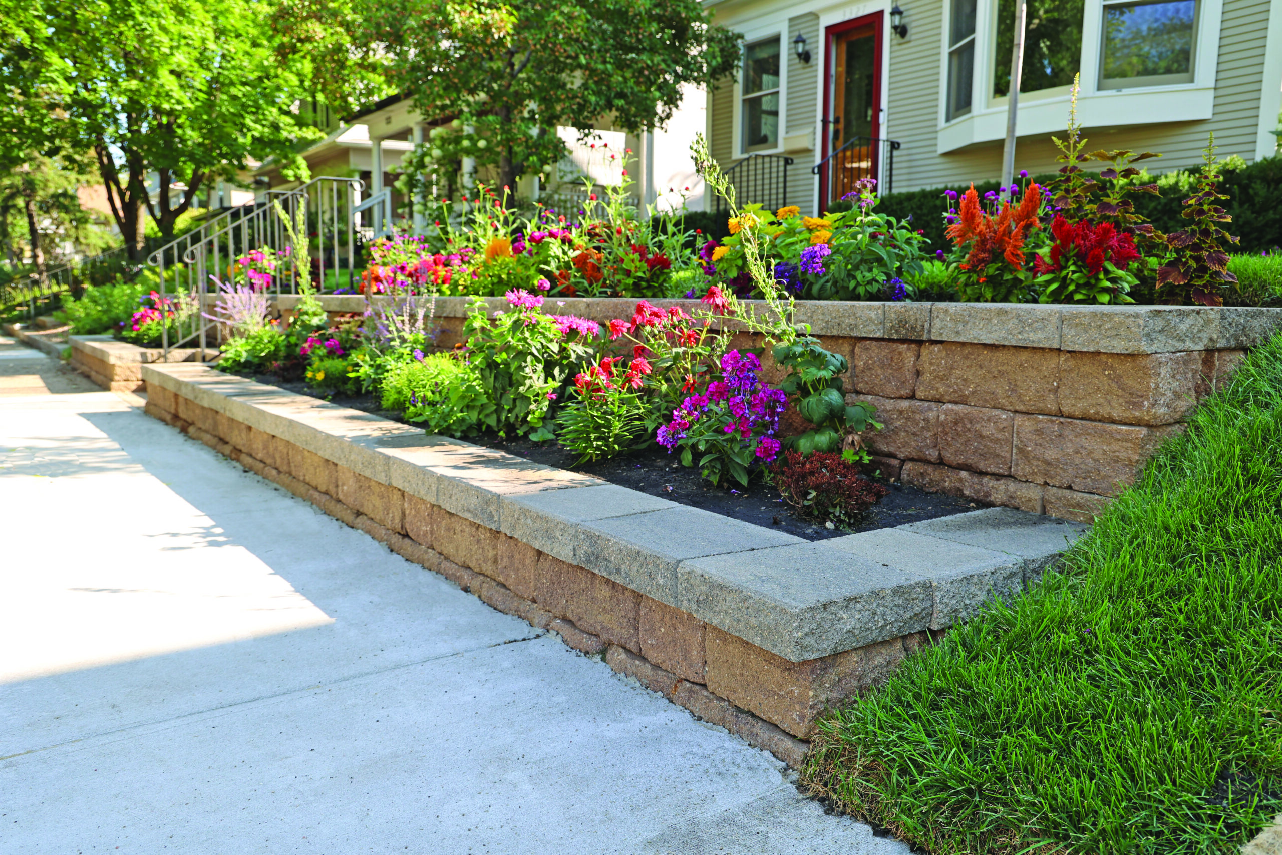 Residential front yard with a tiered stone retaining wall and a colorful flower bed along the walkway