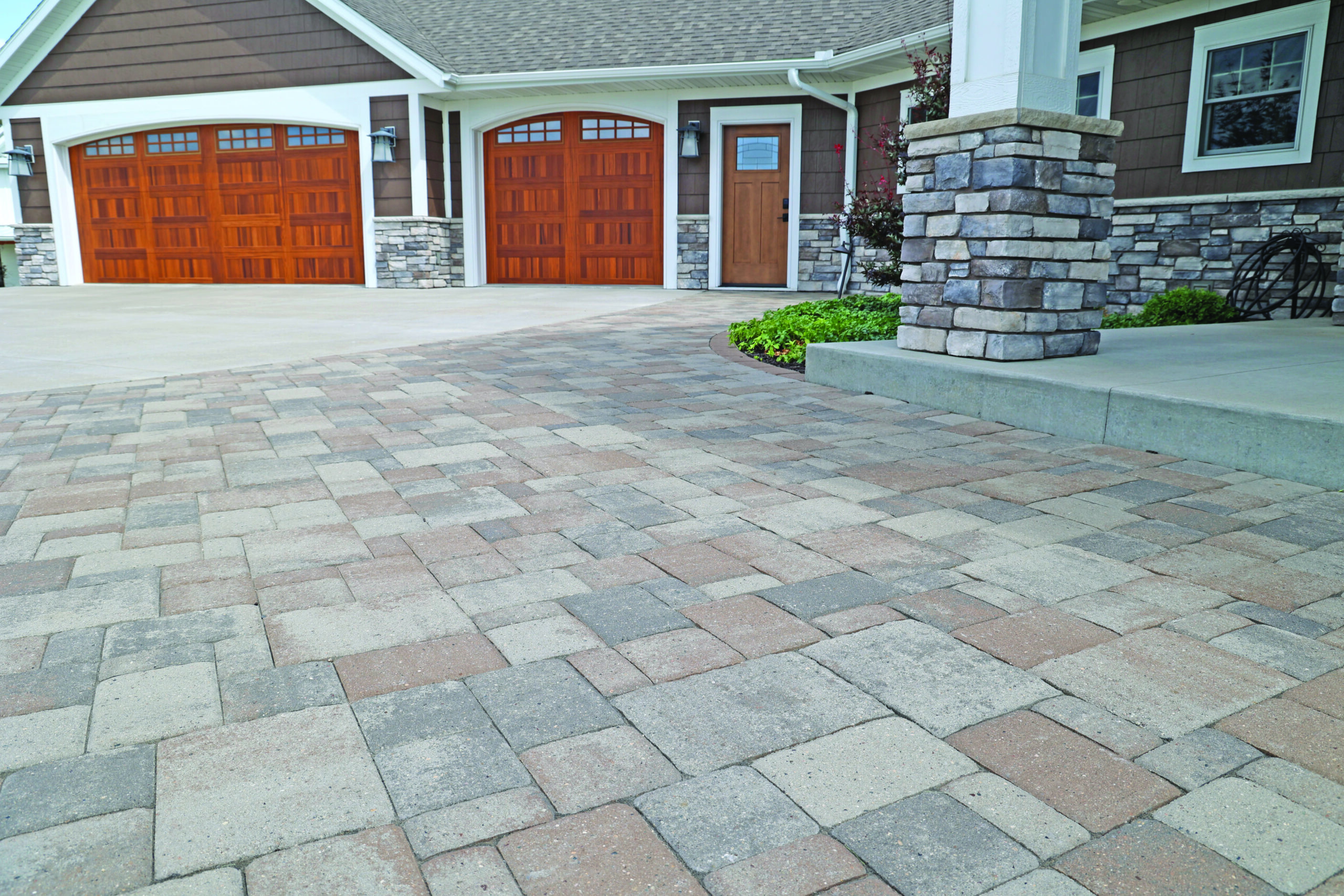 Front view of a house with two wooden garage doors, a wooden entry door, and a stone-accented exterior with a paved driveway.