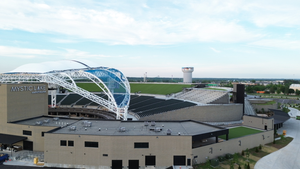 Aerial view of Mystic Lake Amphitheatre: white curved canopy arches over outdoor seating and surrounding buildings nearby.