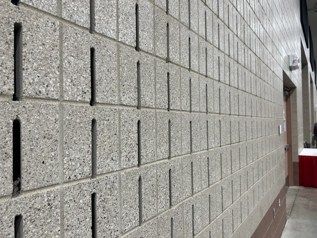 Interior hallway with a long beige block wall featuring vertical slots, extending toward a doorway on the right.