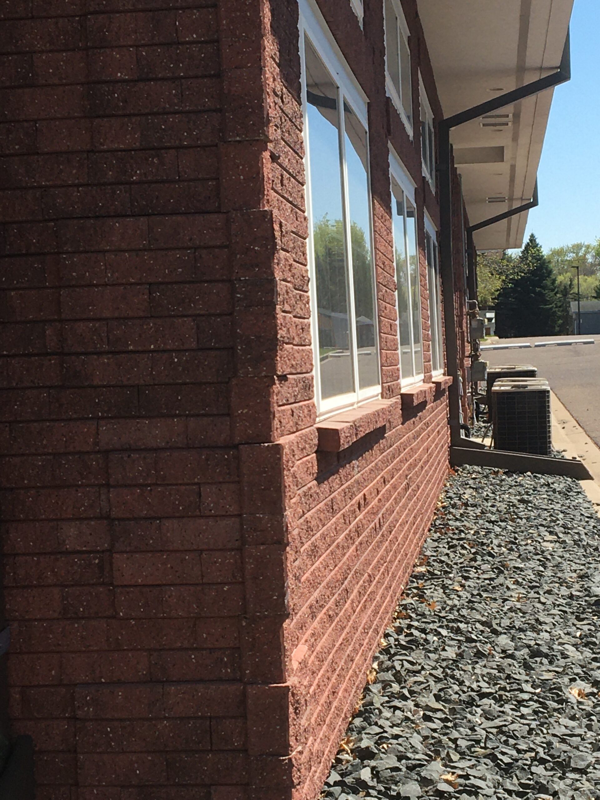 Exterior side of a red brick building with large glass windows along the wall and a gravel path beside it.